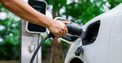 Poignée de main branchant une voiture hybride à une station de recharge avec un paysage de La Réunion en arrière-plan - Véhicules Occasion Réunion