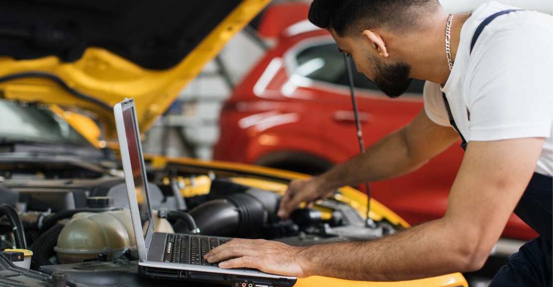 Technicien vérifiant le moteur d’un véhicule d’occasion garanti à La Réunion avec un ordinateur