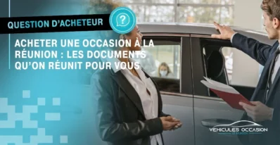 Un vendeur tenant un dossier de documents échange avec une cliente devant une voiture d'occasion à La Réunion